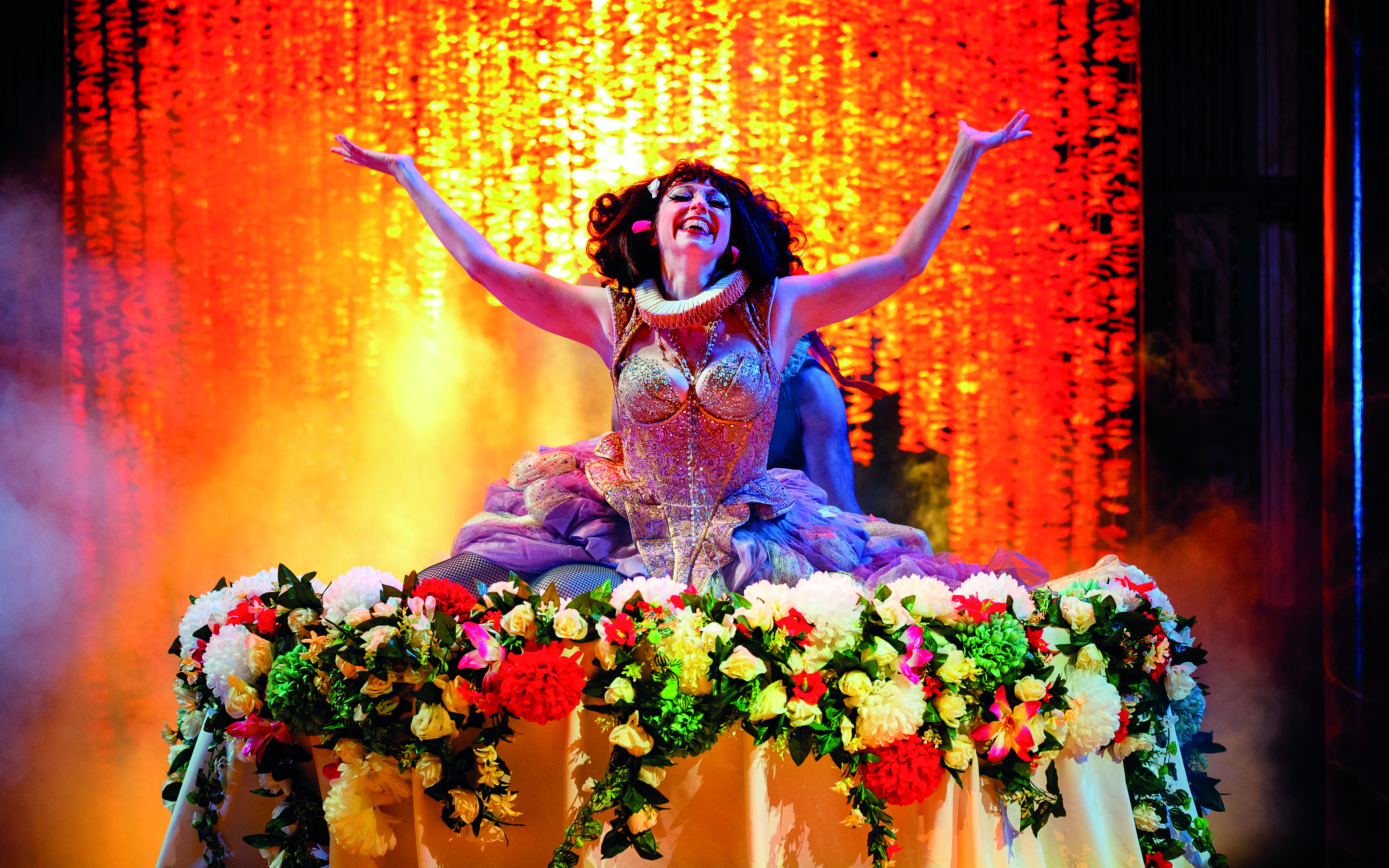 An actor sitting on a table decorated with flowers starring in A Midsummer Night's Dream from the Shakespeare's Globe on Screen 2 collection